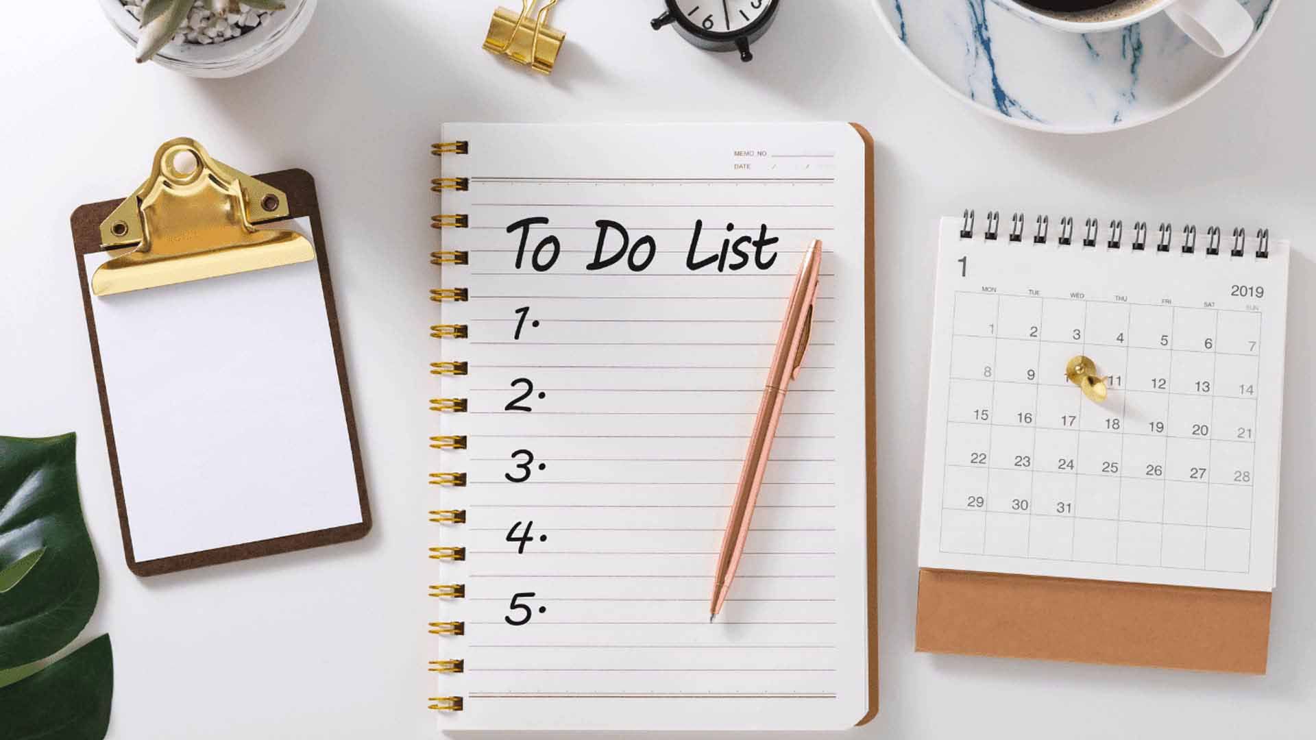 An overhead shot of an organized desk. In the center, a spiral notebook is open to a blank, numbered "To Do List," with a rose-gold pen resting on top. The desk also has a small clipboard, a cup of coffee, and a desk calendar for January 2019.